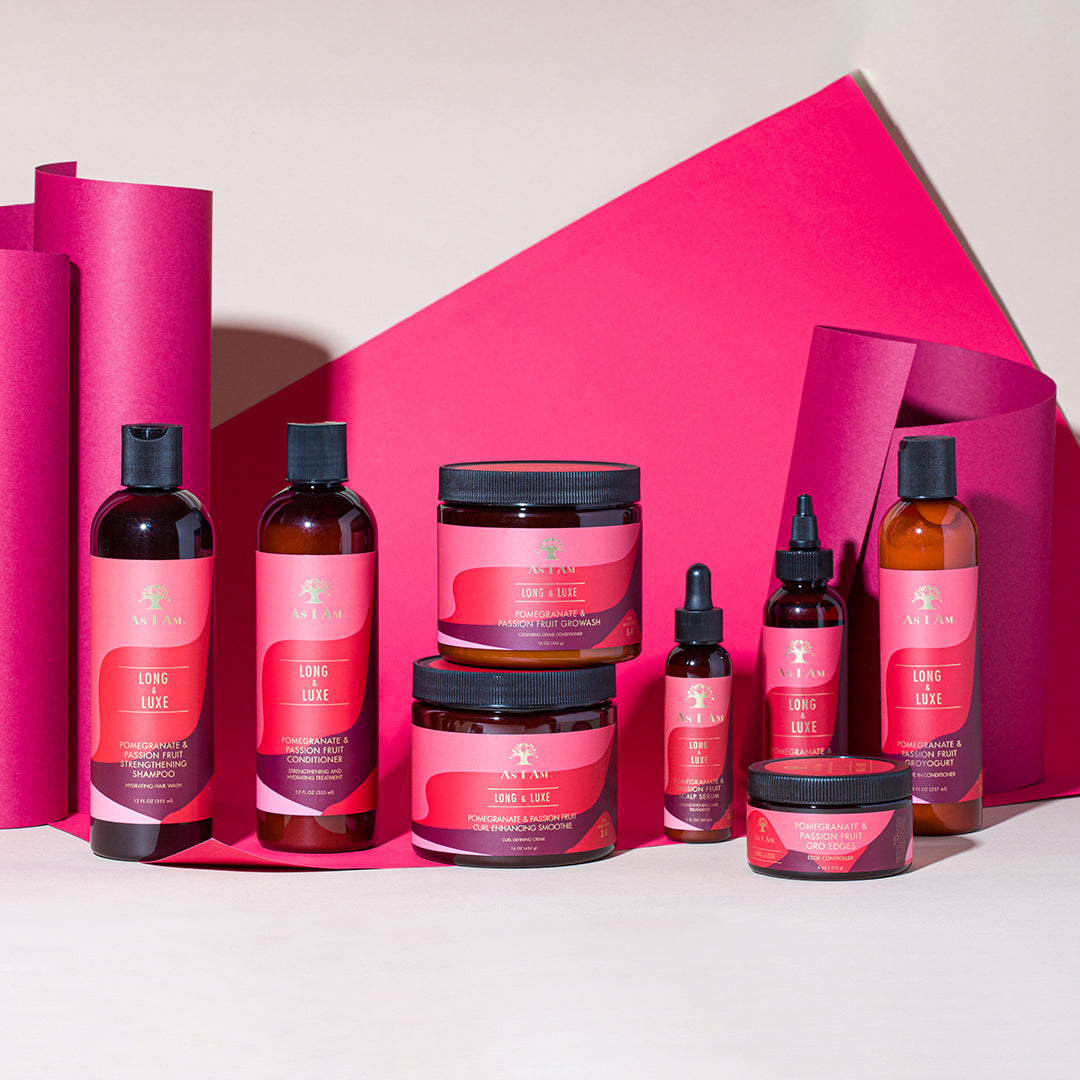 Das Bild zeigt As I Am Long and Luxe Strengthening Shampoo, Conditioner, GroHair Oil und weitere Produkte aus der Serie. Die Produkte sind vor einem rosa Hintergrund angeordnet.
