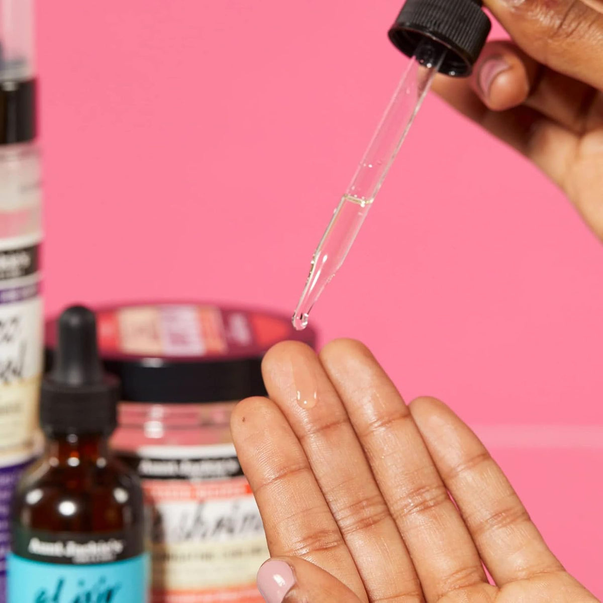 Nahaufnahme einer Hand, die Aunt Jackie's Elixir Biotin Rosemary Hair and Scalp Oil aus einer Pipette auf die Fingerspitze tropft.