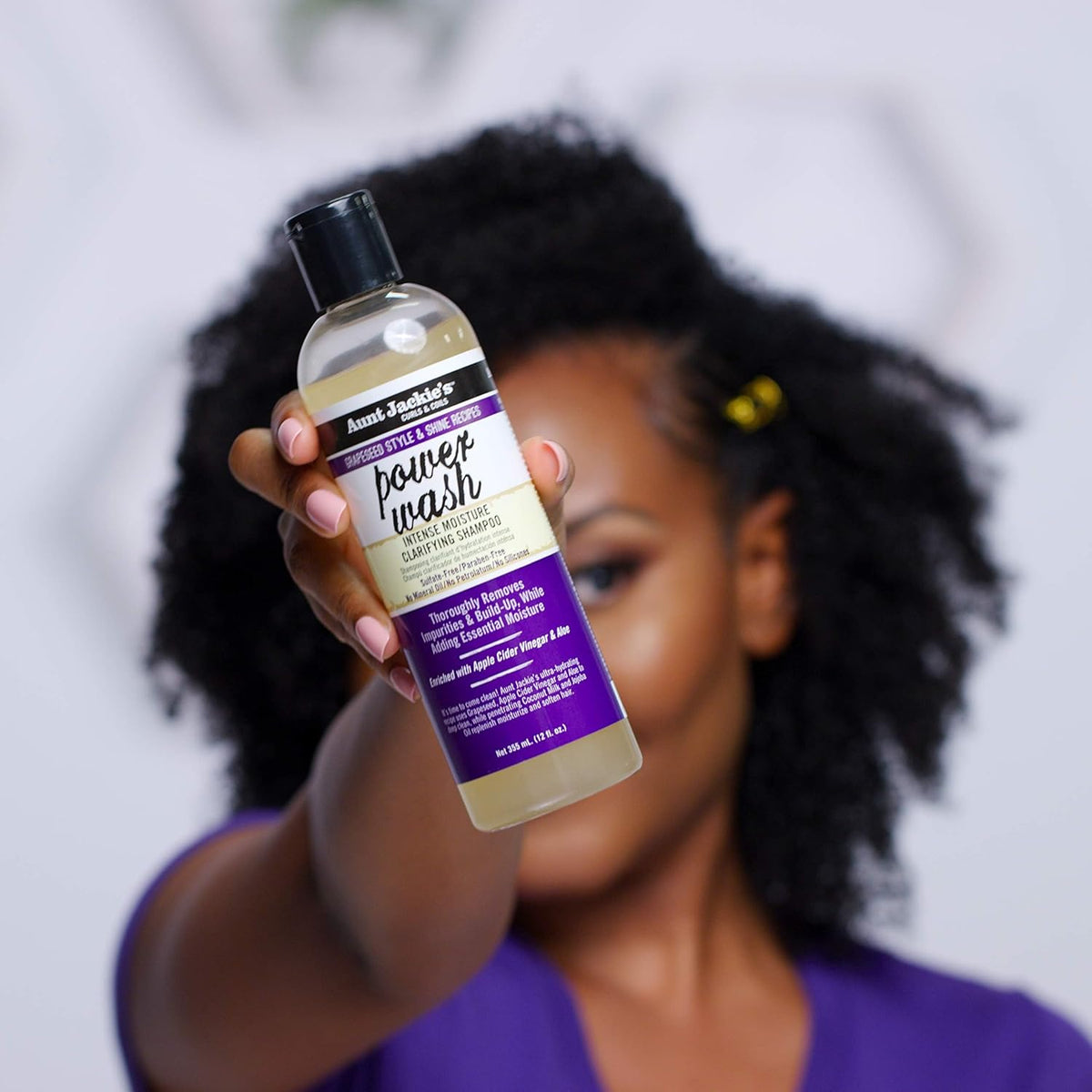 Frau hält eine Flasche Aunt Jackie's Power Wash Intense Moisture Clarifying Shampoo.