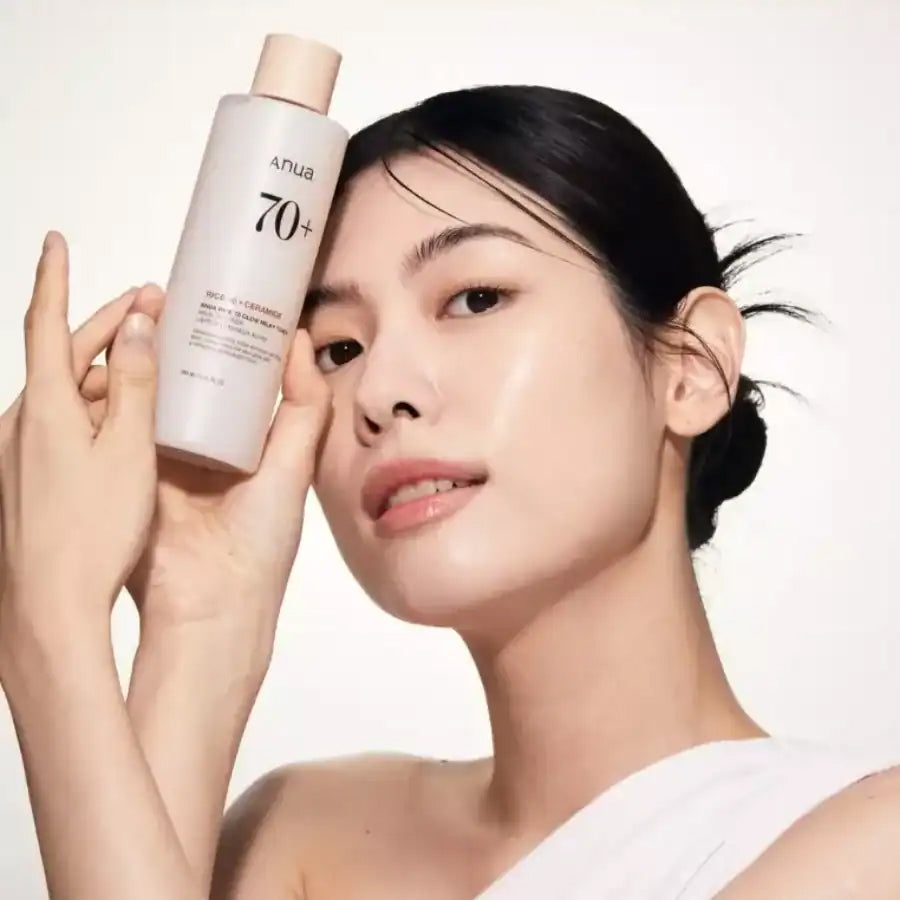 Frau mit strahlender Haut hält Anua Rice 70 Glow Milky Toner 250 ml vor hellem Hintergrund an ihr Gesicht.