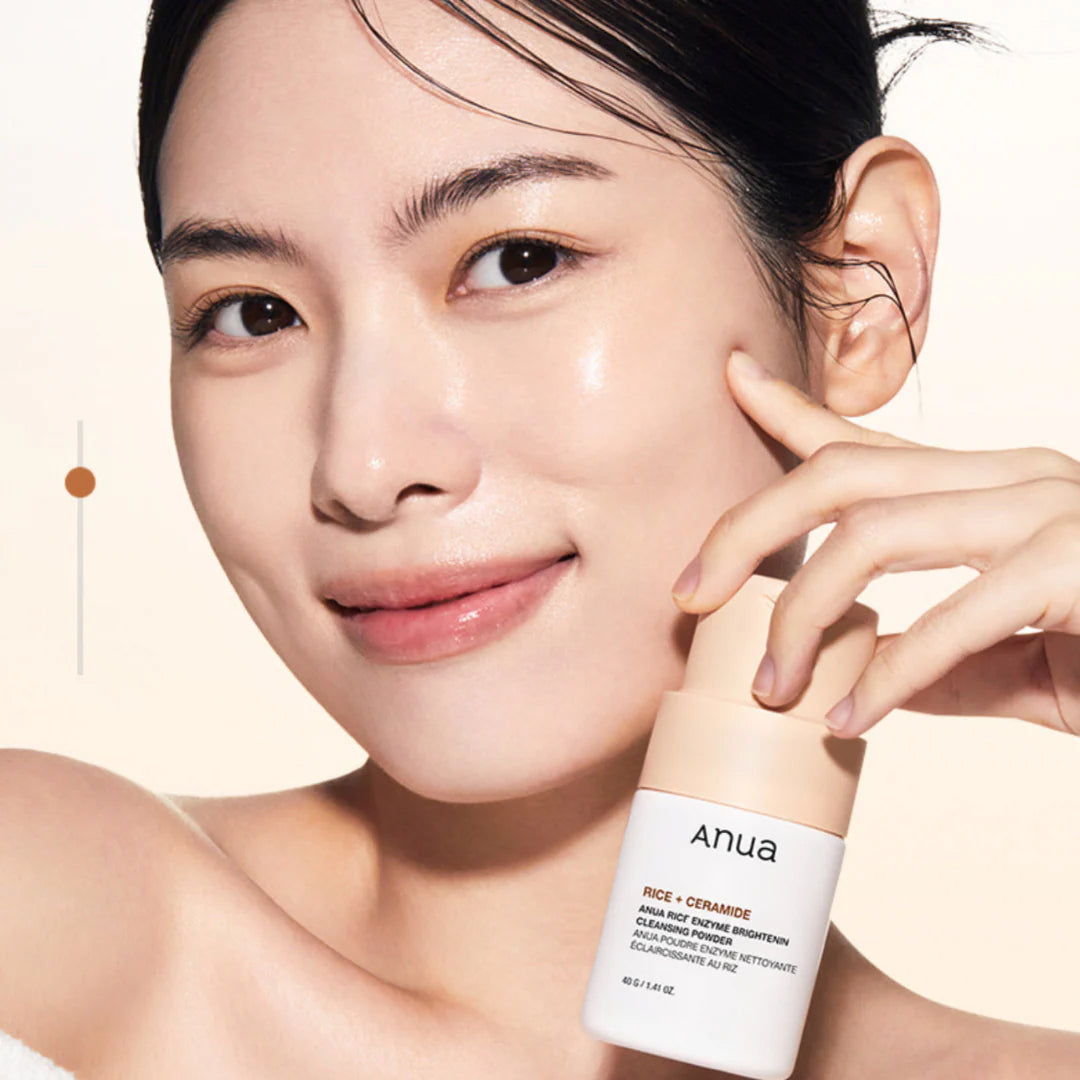 Frau mit strahlender Haut lächelt und hält Anua Rice Enzyme Brightening Cleansing Powder 40gr an ihre Wange.