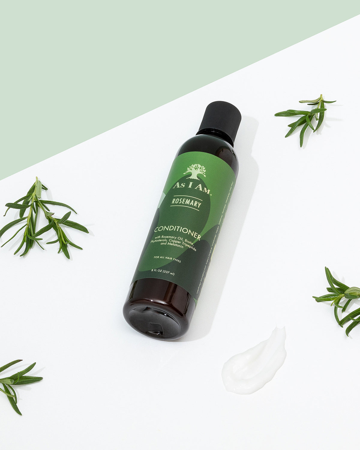 Eine Flasche As I Am Rosemary Conditioner (237 ml) liegt schräg auf einer weißen Oberfläche mit verstreuten Rosmarinzweigen und einem Klecks Conditioner.