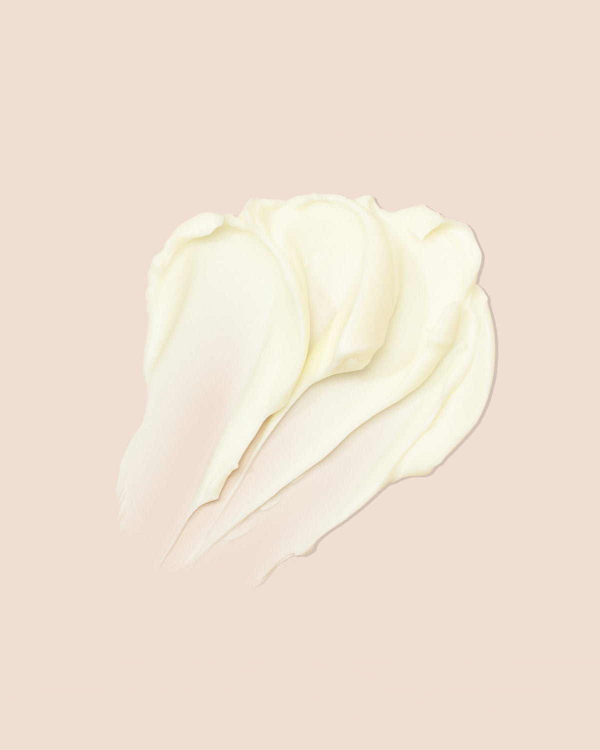 Eine Nahaufnahme eines Kleckses weißer Creme auf rosa Hintergrund. Die Creme wird in weichen, wellenförmigen Linien verteilt. Das Bild zeigt den Inhalt des Produkts As I Am Classic DoubleButter Cream.