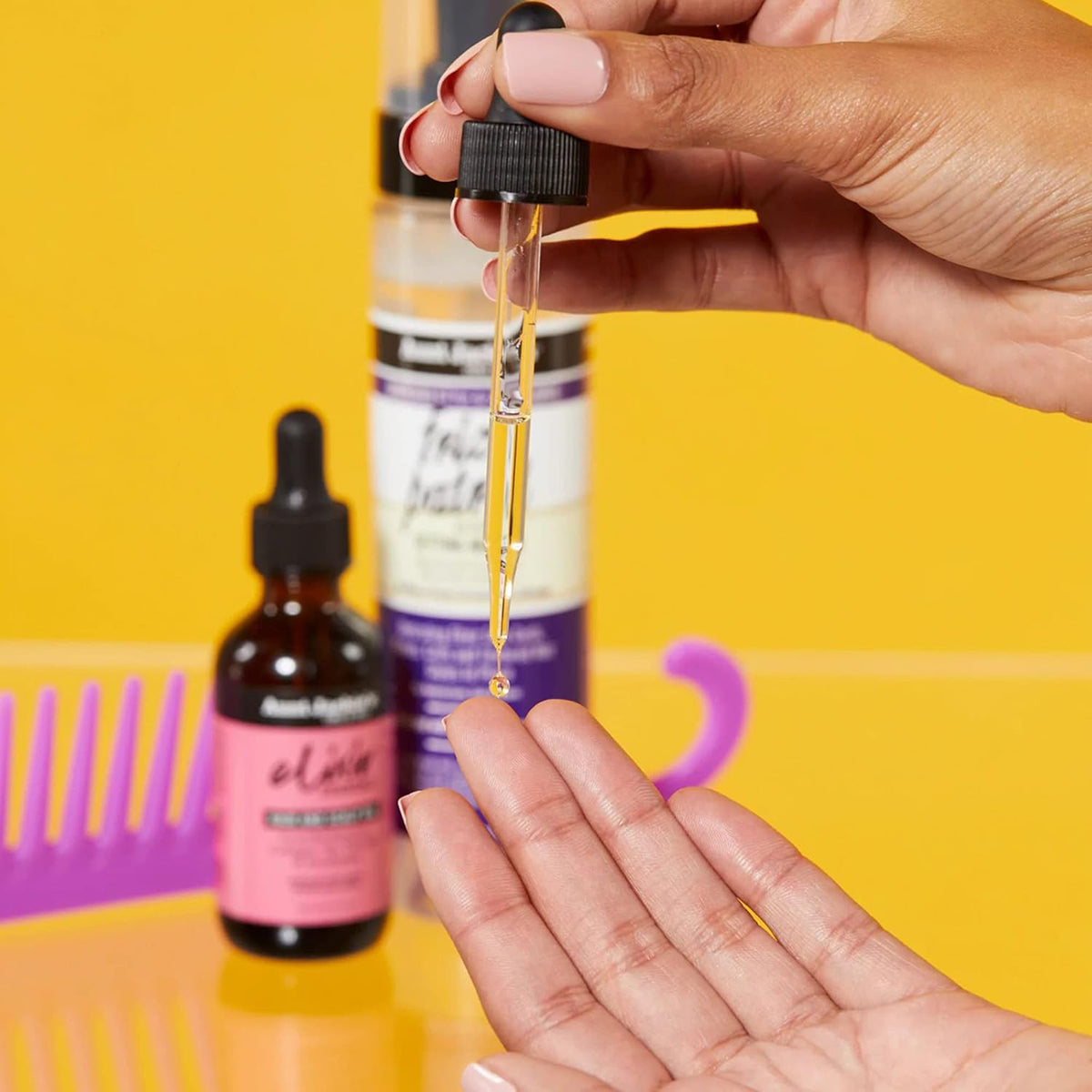 Nahaufnahme von Tante Jackies Elixir-Haaröl, das aus der Pipette in eine Hand tropft.