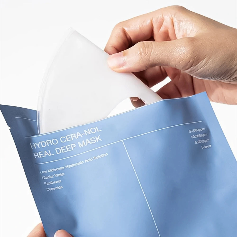 Die Hand nimmt die Biodance Hydro Cera-nol Real Deep Mask aus der blauen Verpackung mit sichtbarer weißer Tuchmaske.