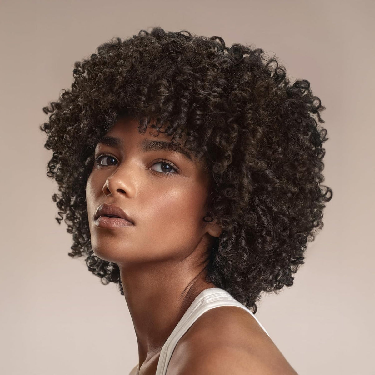 Frau mit natürlich gelocktem dunkelbraunem Afro-Haar und Vorhang-Pony, trägt weißes Leinen.