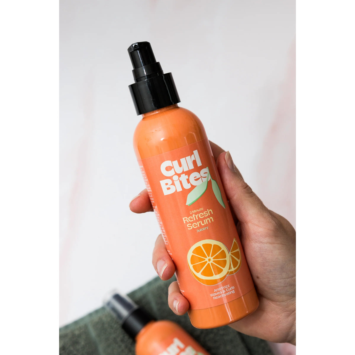 Hand hält Curl Bites 2 Minute Refresh Serum, orangefarbene Flasche mit Pumpe und orangefarbenem Motiv.