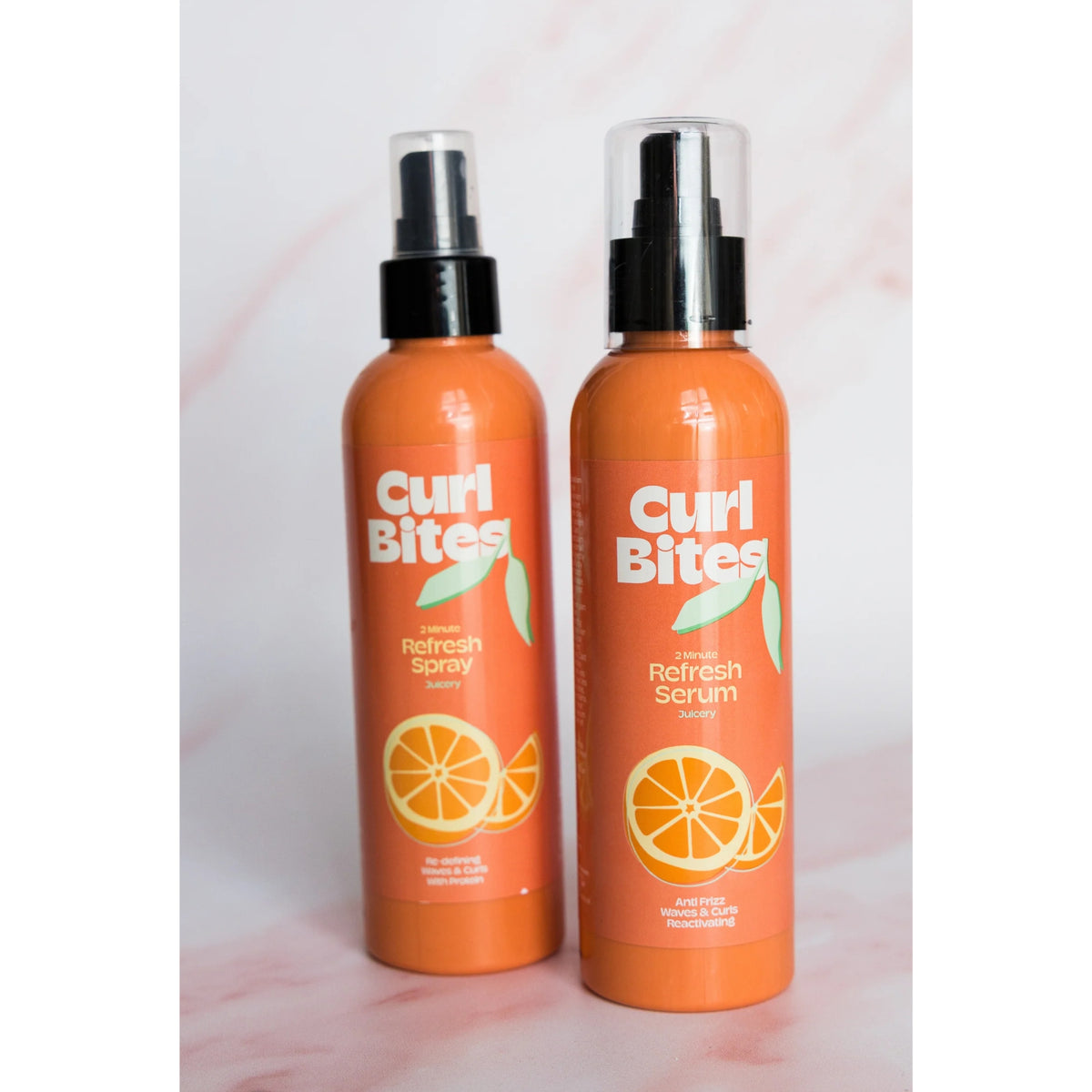 Zwei orangefarbene Curl Bites-Flaschen: 2 Minute Refresh Spray und Refresh Serum mit orangefarbenem Motiv auf rosa Hintergrund.