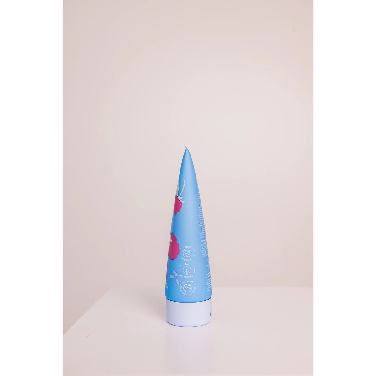 Kegelförmige blaue Röhre mit rosa Blüten, weißer Deckel, stehend auf weißer Tischplatte.
