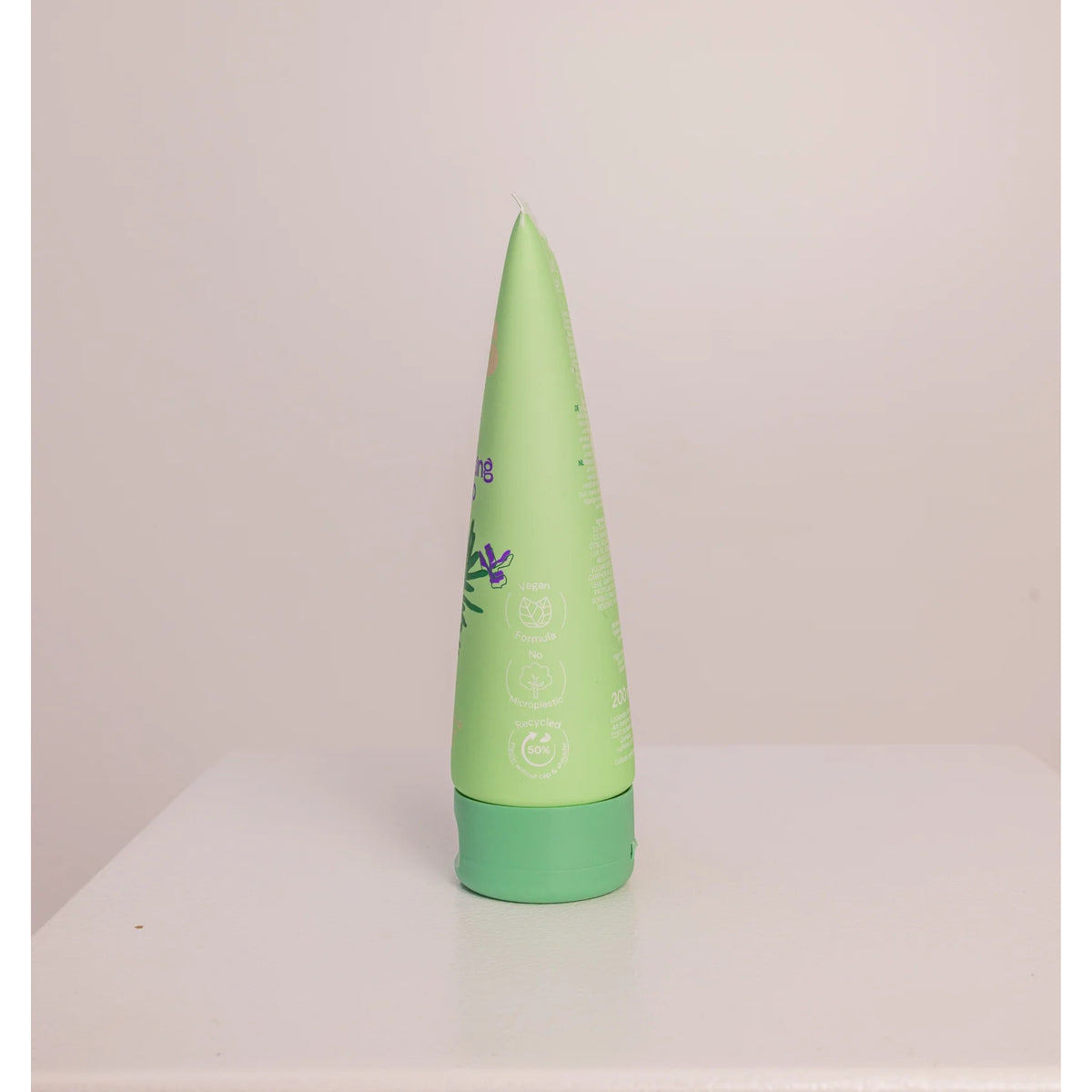 Grünes Tubenshampoo mit grünem Deckel, veganer und recycelter Kunststoff, aufrecht stehend auf weißer Tischplatte.