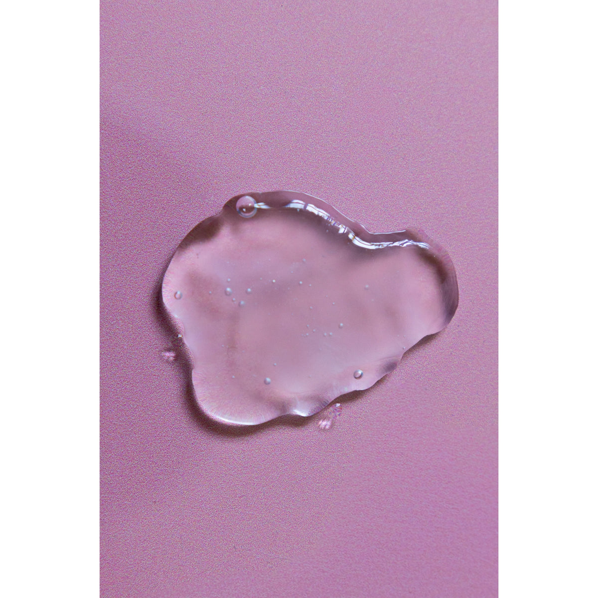 Transparente Geltextur mit Luftblasen auf rosa Hintergrund, die die Konsistenz eines Hautpflegeserums zeigt.