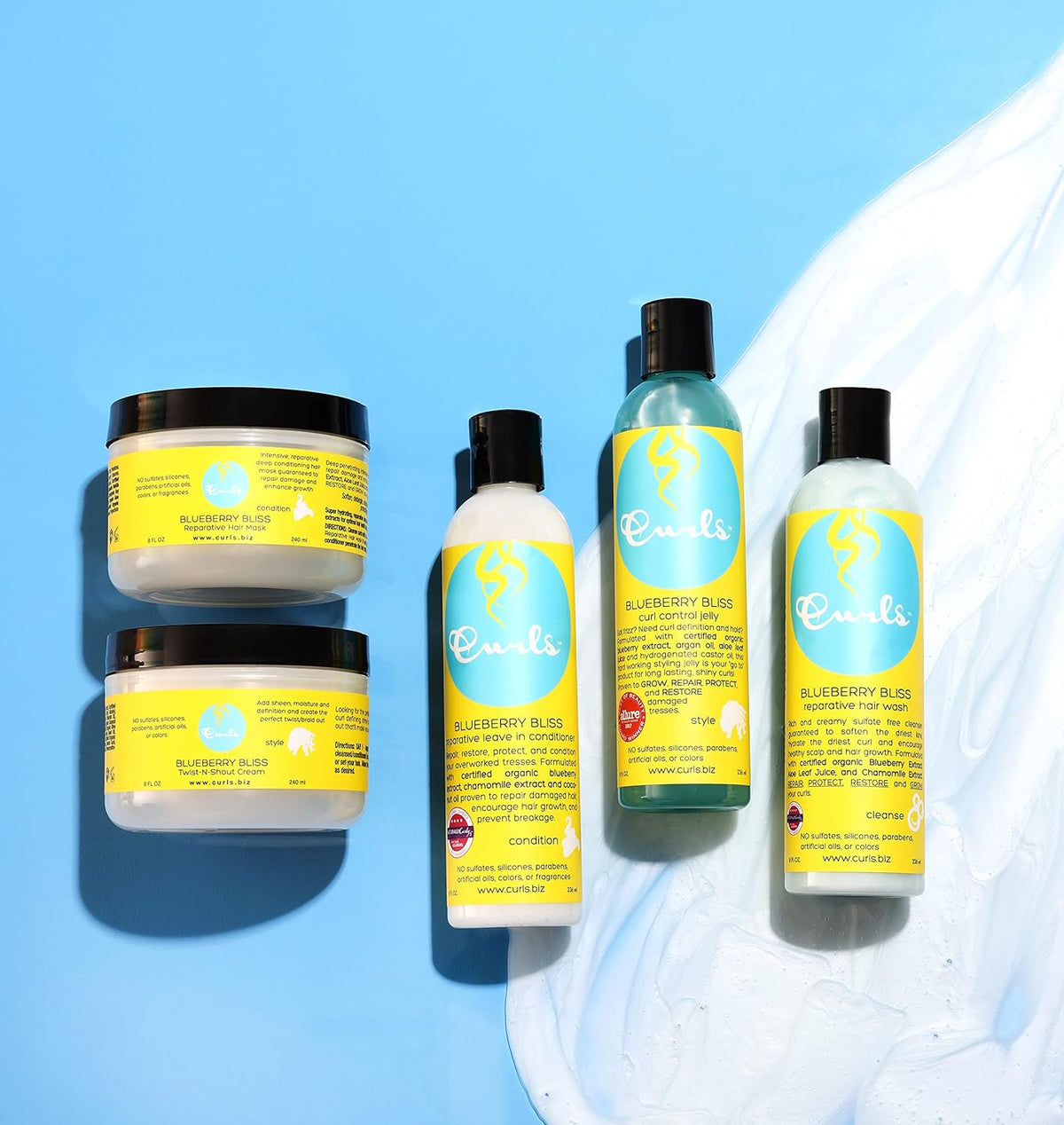 Four Curls Blueberry Bliss-Produkte: Zwei Gläser Gelee/Paste, eine Flasche Öl und eine Flasche Leave-in-Conditioner auf hellblauem Hintergrund.