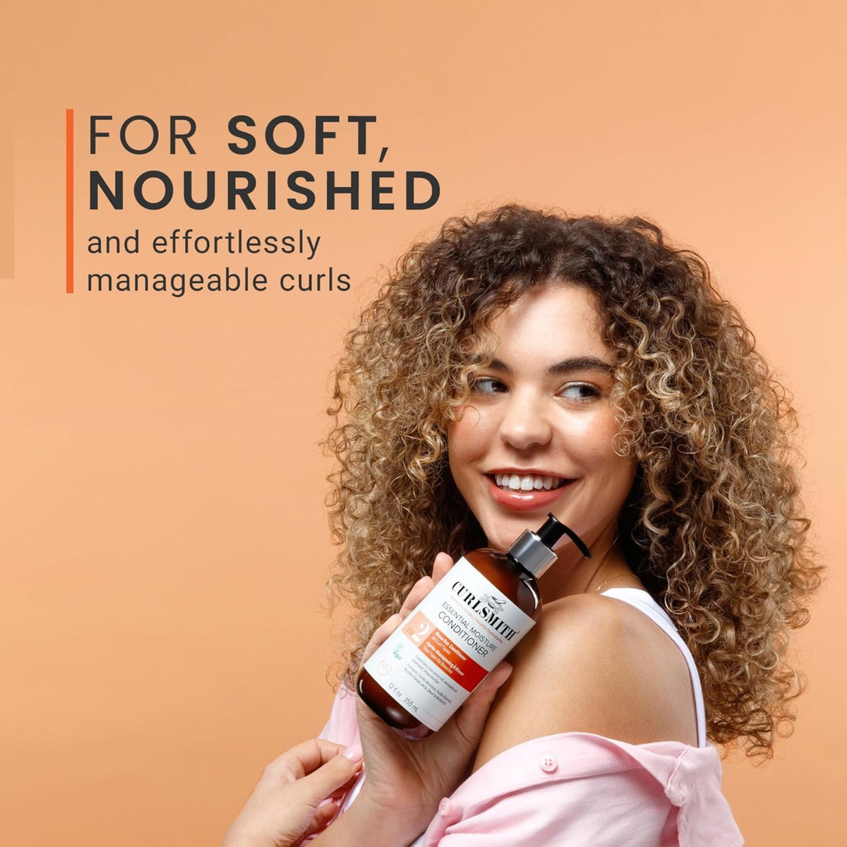 Frau mit weichen, gepflegten Locken hält Curlsmith Essential Moisture Conditioner an ihre Schulter und lächelt.