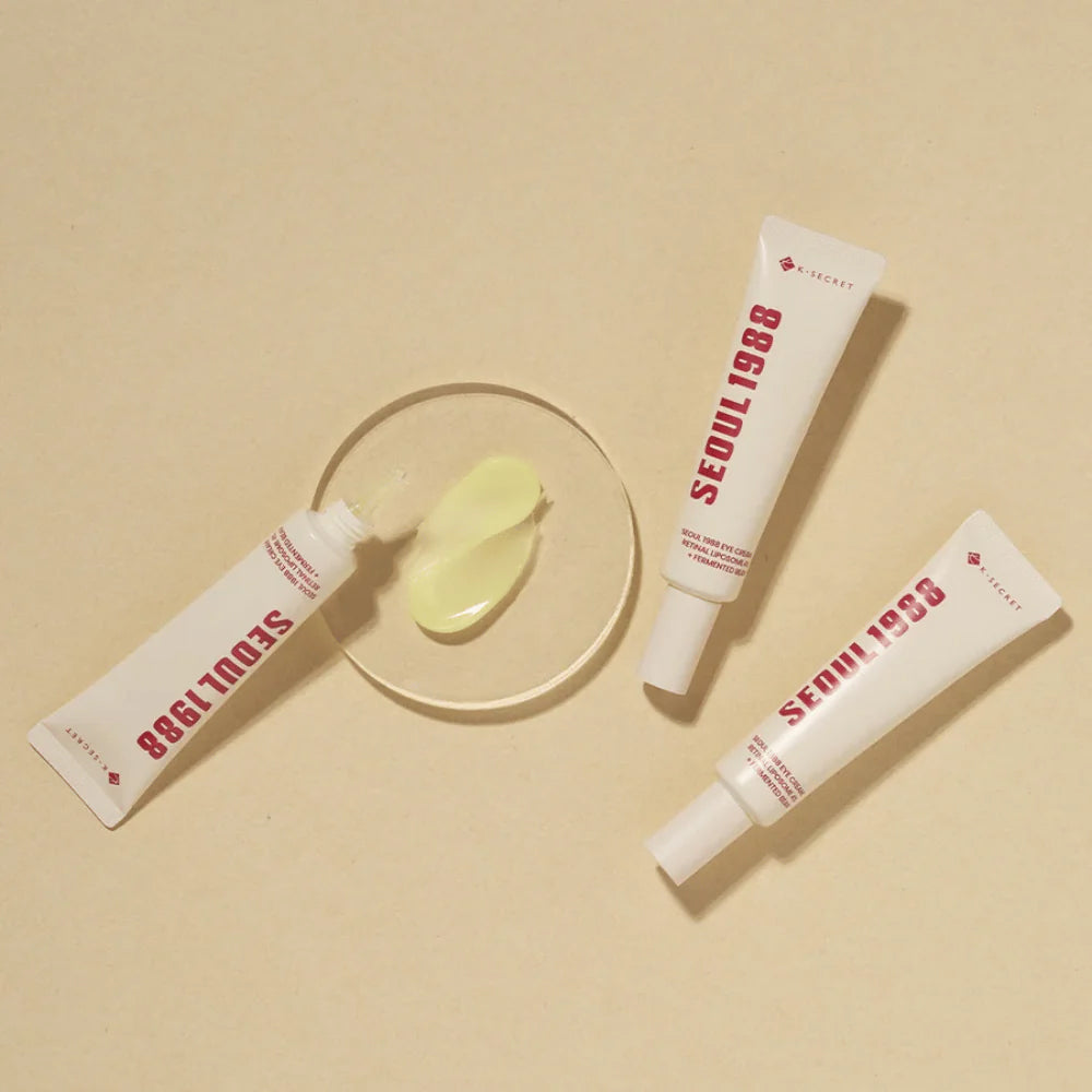 Drei Tuben K-Secret Eye Cream: Retinal Liposome 4 % + Fermented Bean 30 ml liegen auf einem beigen Hintergrund mit der Creme in der Mitte.