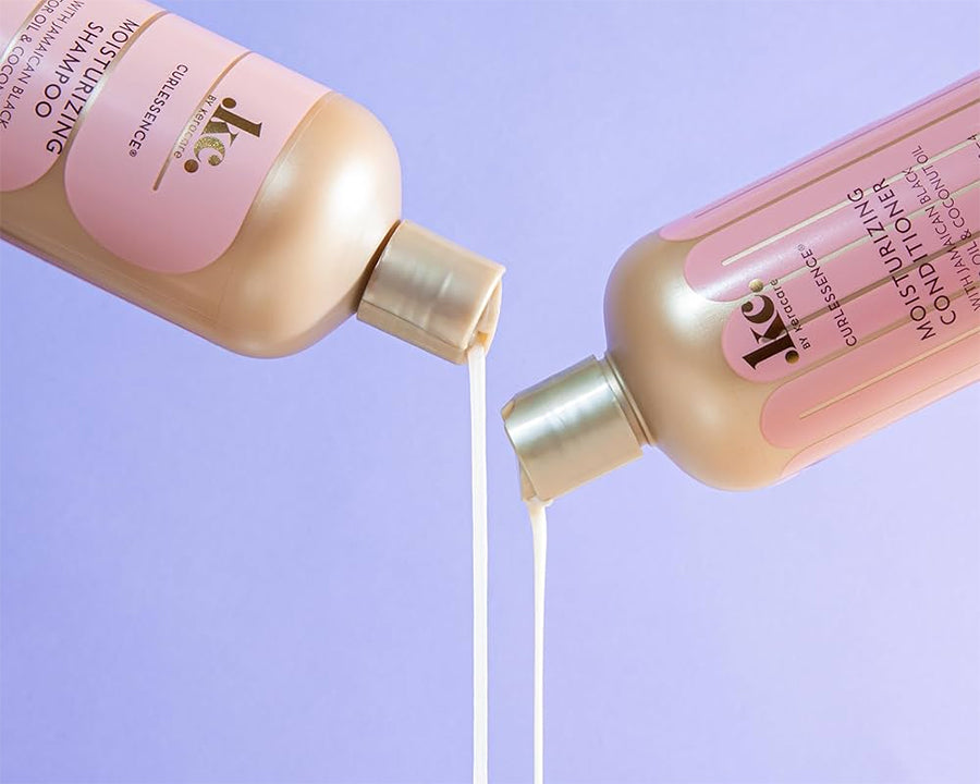 Keracare Curlessence Moisturizing Shampoo und Moisturizing Conditioner werden vor einem violetten Hintergrund gegossen.