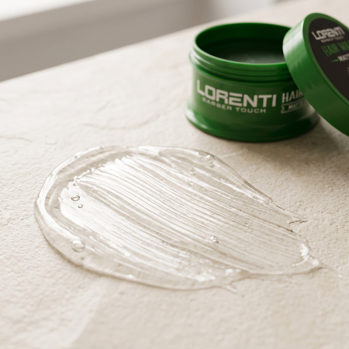 Lorenti Barber Touch hair wax i åben grøn dåse med klar, gelagtig konsistens smurt ud på lys stenoverflade.