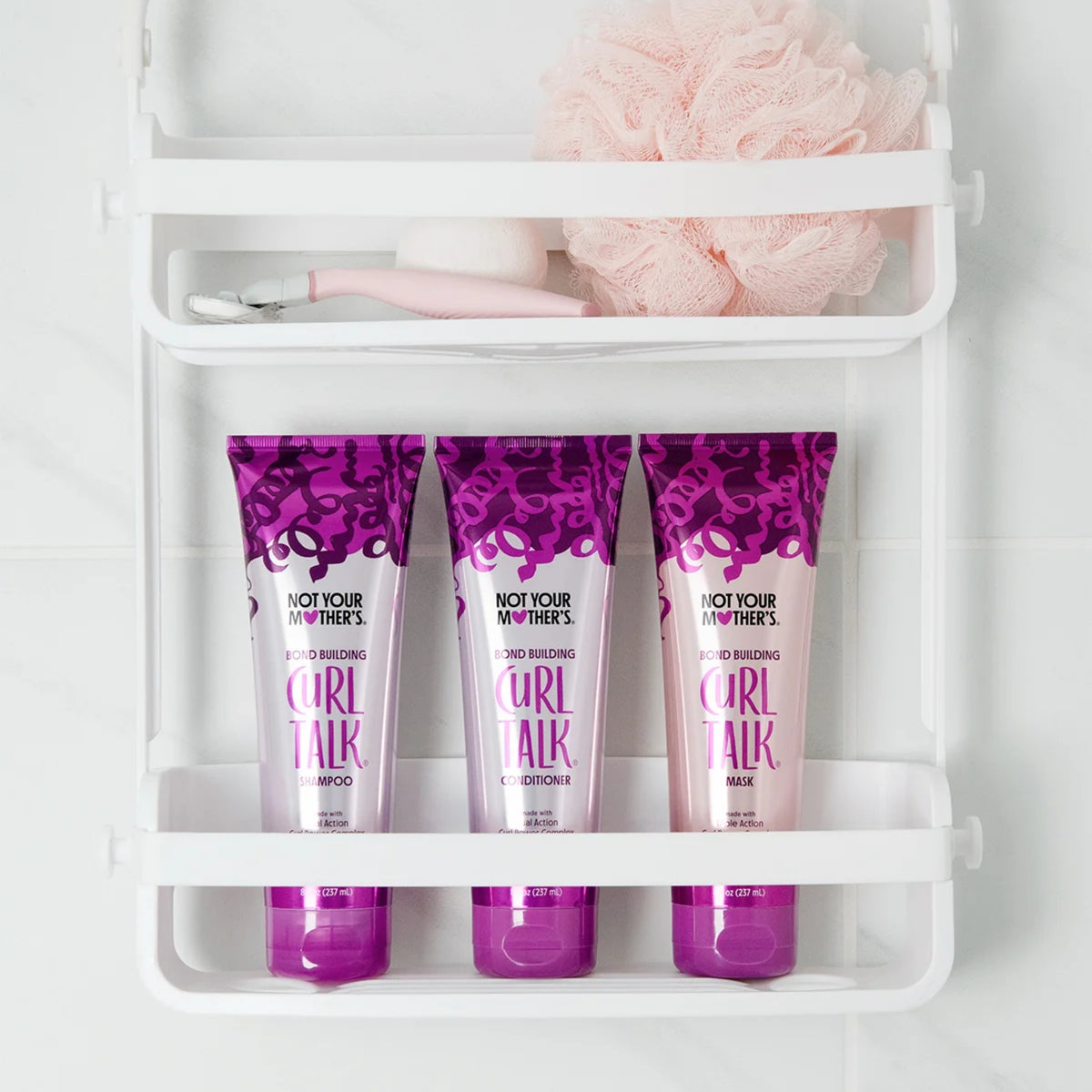 Not Your Mother's Curl Talk shampoo, conditioner og maske i lilla tuber på hvid badehylde med pink svamp.