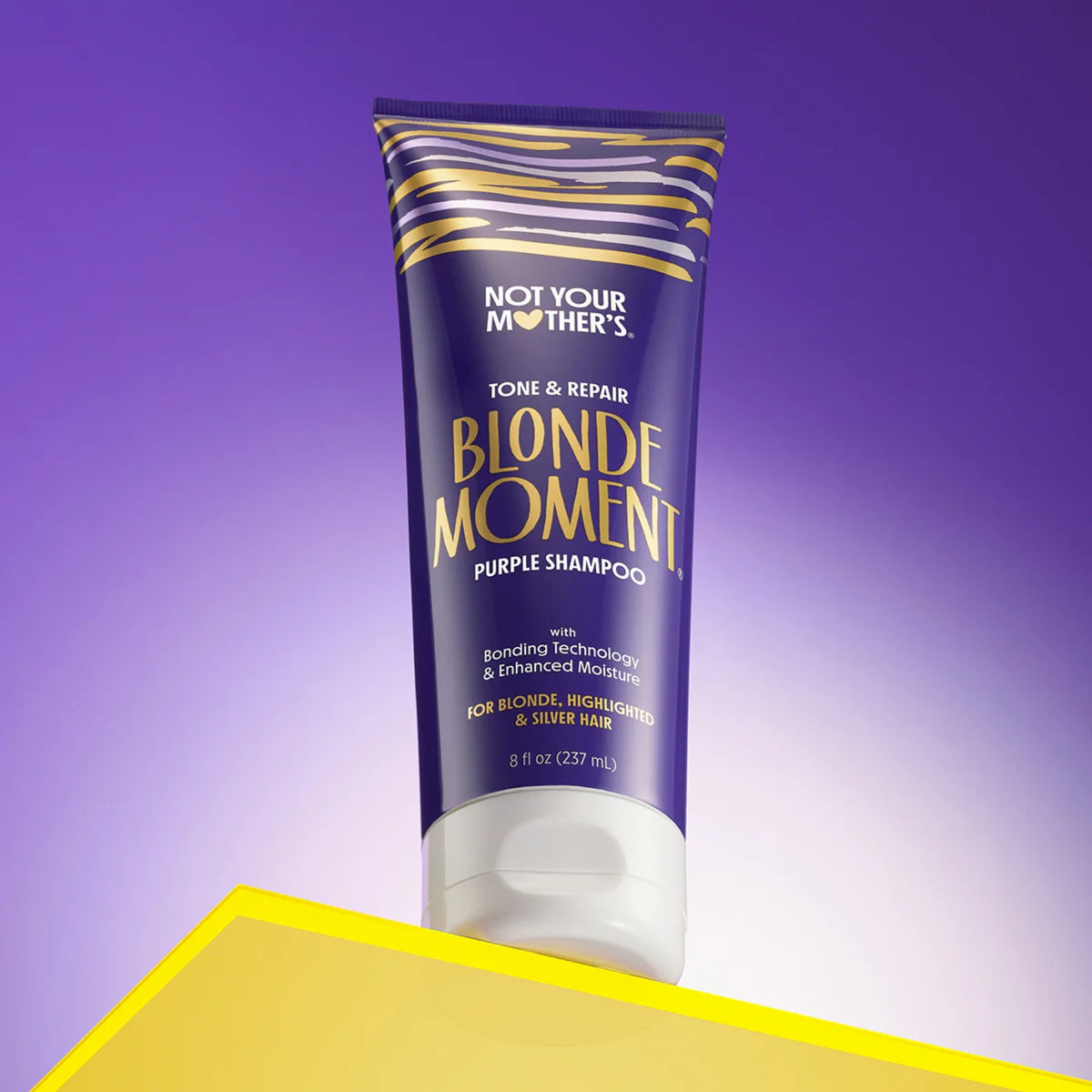 Not Your Mother's Blonde Moment lila Shampoo für blondes Haar in lila und goldener Tube auf gelbem Tisch.