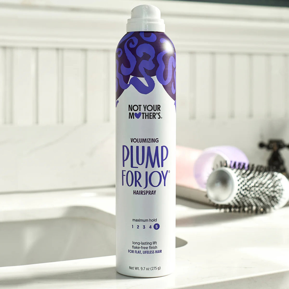 Das voluminöse Haarspray „Not Your Mother's Plump For Joy“ in Lila und Weiß kann mit einer Rundbürste auf das Waschbecken im Badezimmer geklebt werden.