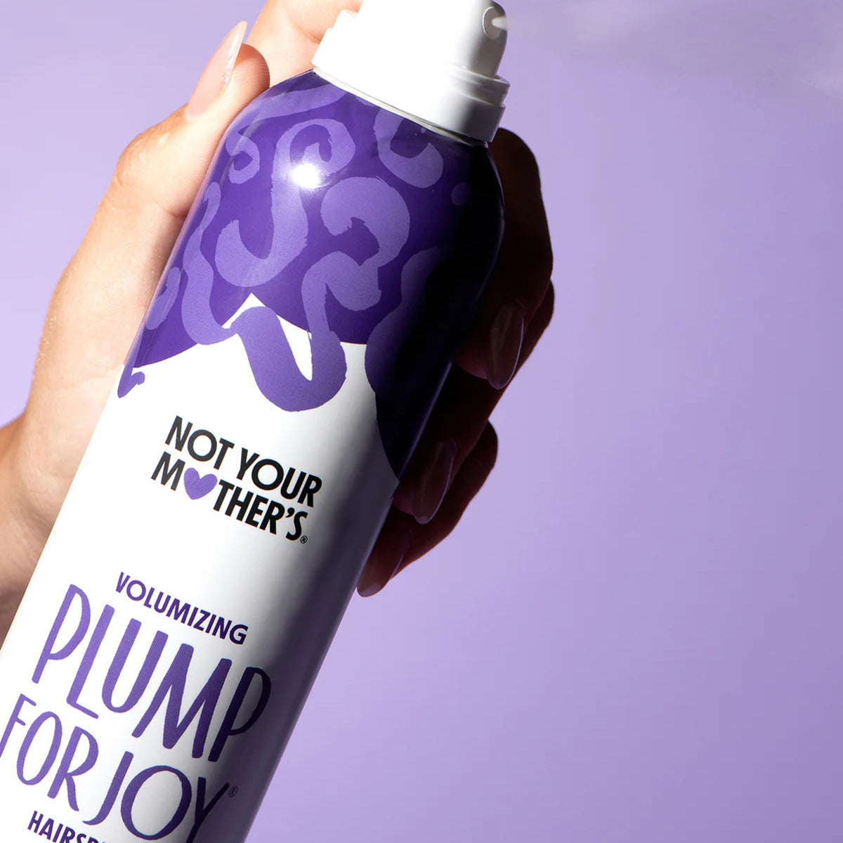 Hand hält Not Your Mother's Plump For Joy voluminöses Haarspray in Lila und Weiß vor violettem Hintergrund.