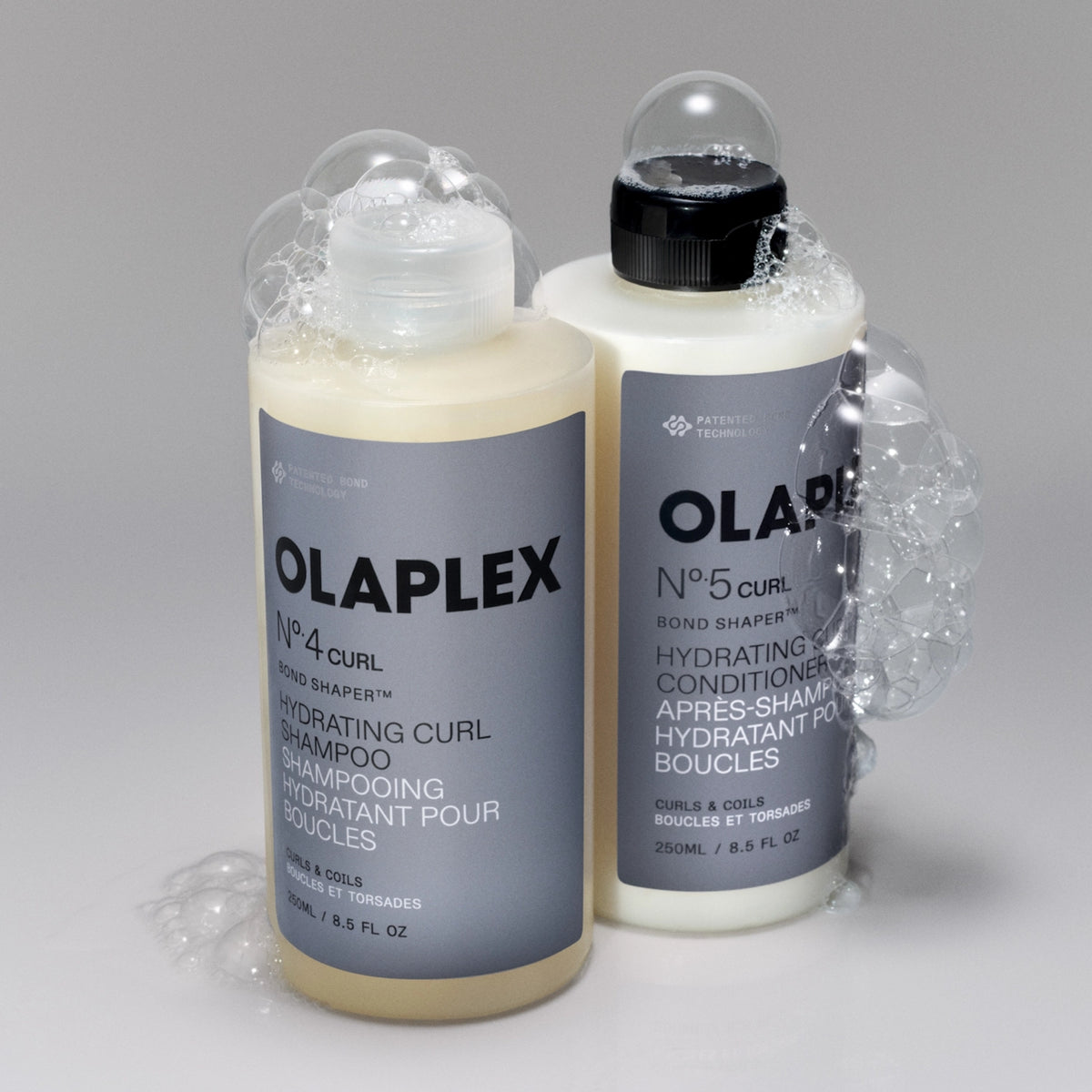 Olaplex No.4 Curl Shampoo und No.5 Curl Conditioner in 250 ml Flaschen umgeben von Schaum.