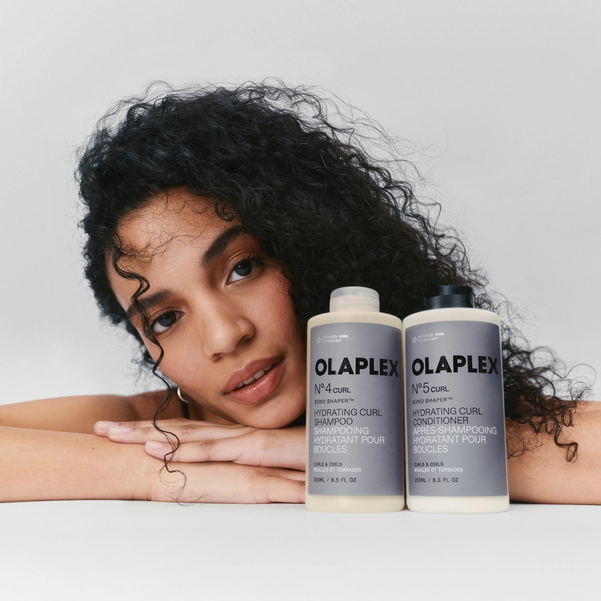 Frau mit lockigem Haar neben Olaplex Nº.4 Curl Shampoo und Nº.5 Curl Conditioner für Boucler.