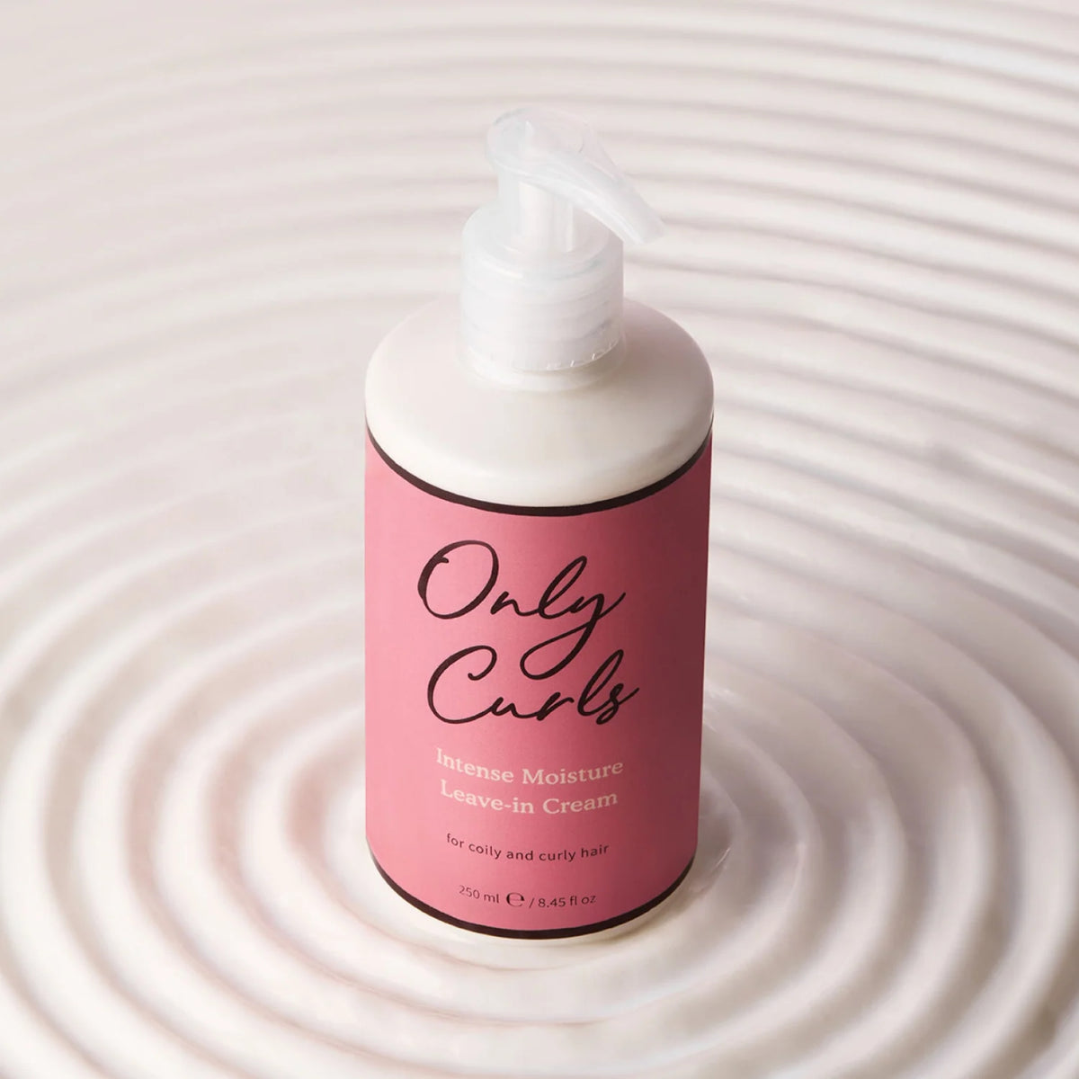 Only Curls Intense Moisture Leave-in Cream, hvid pumpeflaske med pink etiket, 250 ml, på lyst vandkruset baggrund.