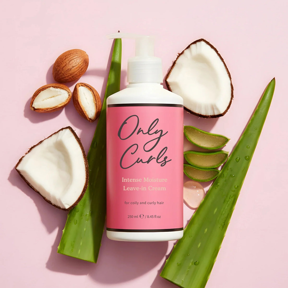 Only Curls Intense Moisture Leave-in Cream flaske omgivet af kokosnød, aloe vera og sheasmør på lyserosa baggrund.