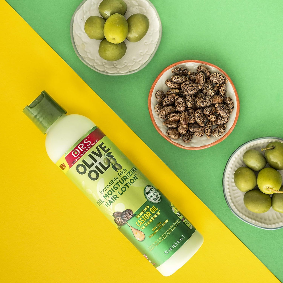 ORS Olive Oil Incredably Rich Oil Moisturizing Hair Lotion umgeben von Oliven und Rizinussamen, die die natürlichen Inhaltsstoffe veranschaulichen.