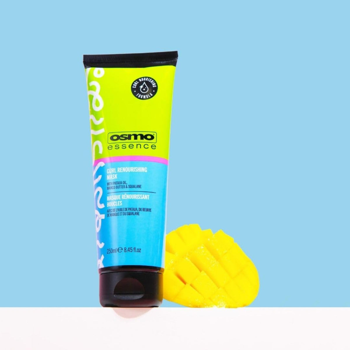 Osmo Essence Curl Renourishing Mask Tube mit 250 ml mit einer geschnitzten Mango daneben auf hellblauem Hintergrund.