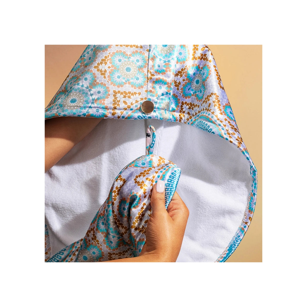 Hände faltender Bounce Curl Satin-Mikrofaser-Turban mit weißer Innenseite und buntem Muster in Blau, Gold und Braun.