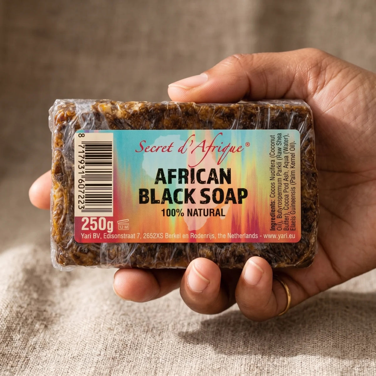Hand hält Secret d'Afrique African Black Soap, 250-g-Seifenstück mit natürlichem dunklem Aussehen und Etikett.